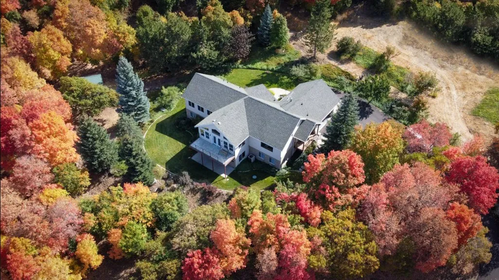 Aerial view of a large residential home nestled among vibrant autumn trees with red, orange, and yellow foliage.