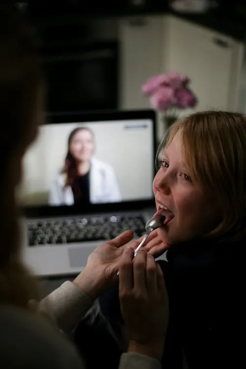 A working parent speaking with a doctor on a laptop while a child sits nearby