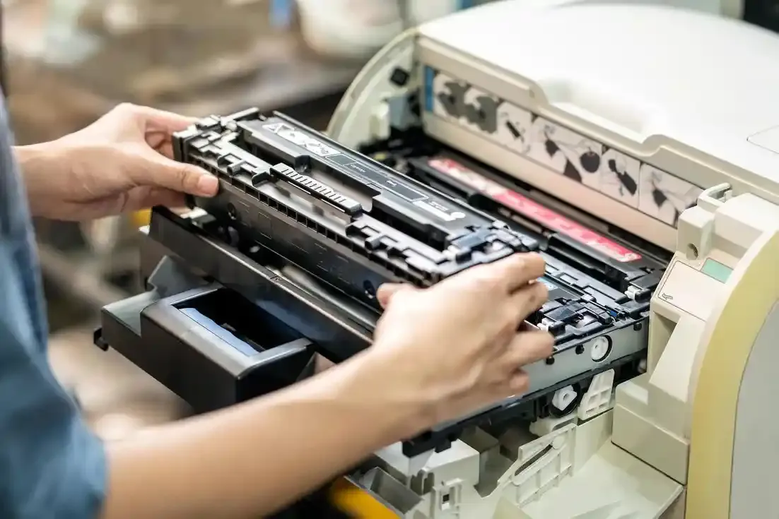 Hands removing or installing a toner cartridge in a laser printer for maintenance or repair.