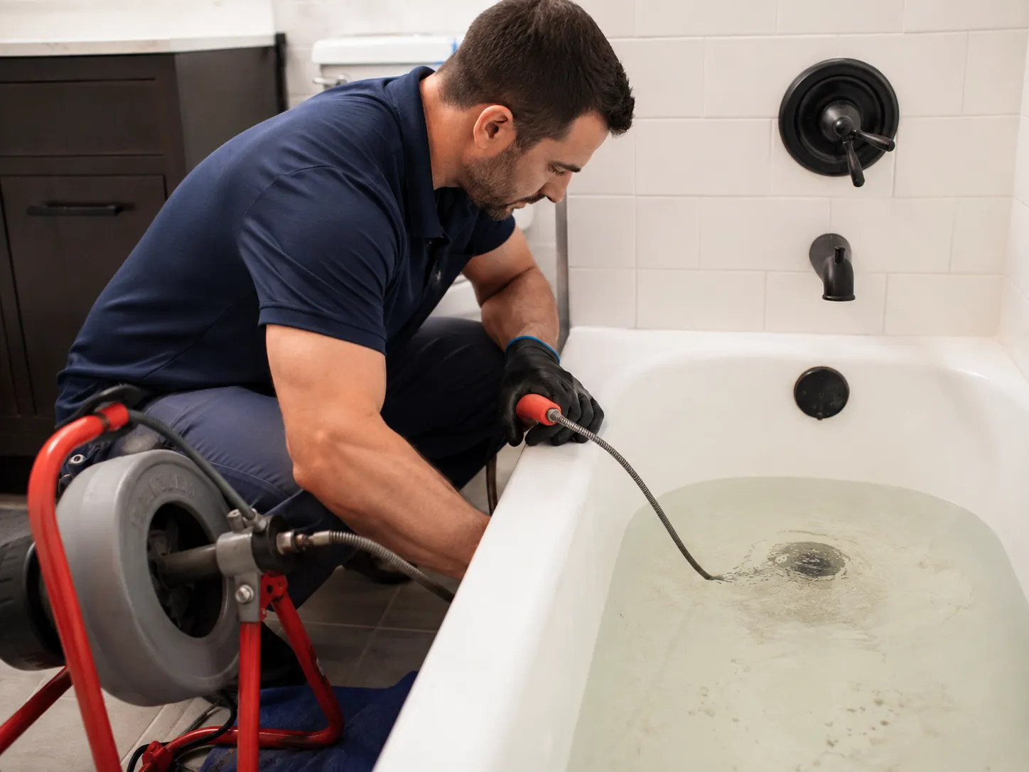 Plumber using drain cleaning equipment to clear a bathtub drain blockage