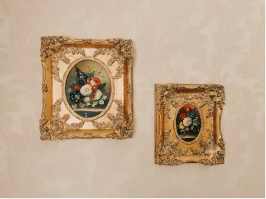 Two ornate gold-framed floral paintings displayed on a textured wall.