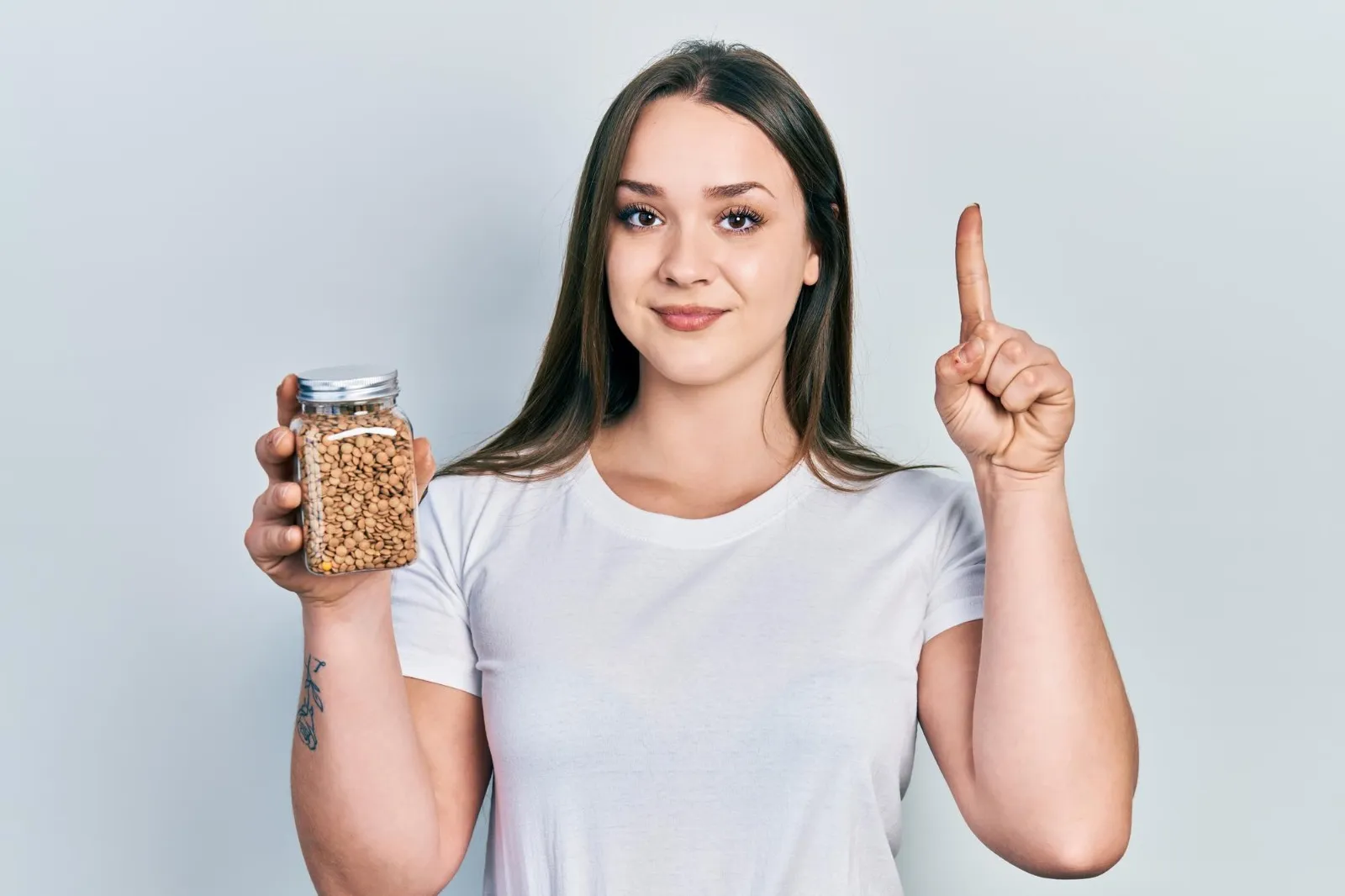 A woman holding a jar of soybeans and pointing upward, representing interest in fermented soybeans, Japanese natto, and healthy lifestyle choices.