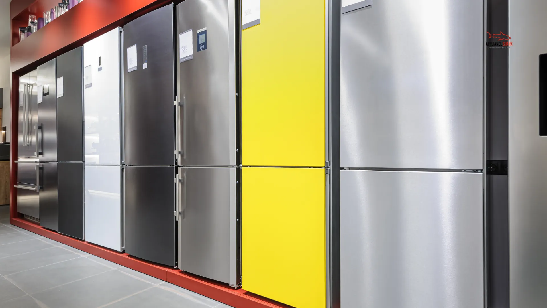 Row of modern refrigerators in various colors and finishes, including stainless steel, black, white, and yellow, displayed in a bright showroom