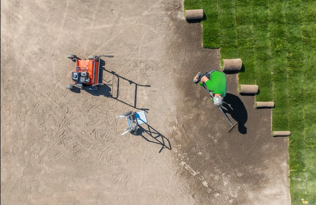 Landscaper installing a new lawn with grass sod rolls and equipment.