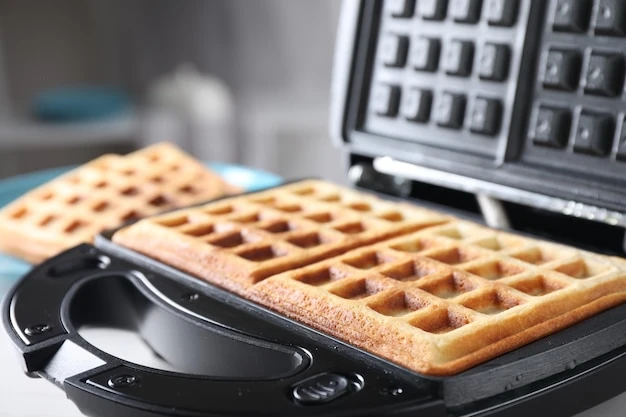 Modern iron with tasty Belgian waffles on table closeup