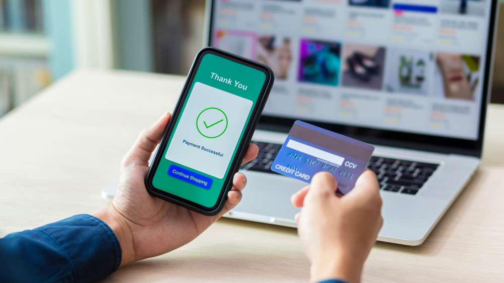 A person holding a smartphone showing a successful payment and a credit card in the other hand. 