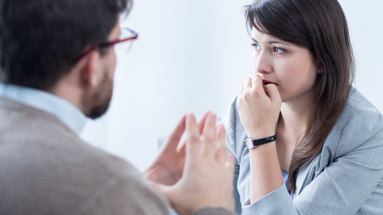 A man gestures with his hands while talking to a woman, who looks concerned and thoughtful.