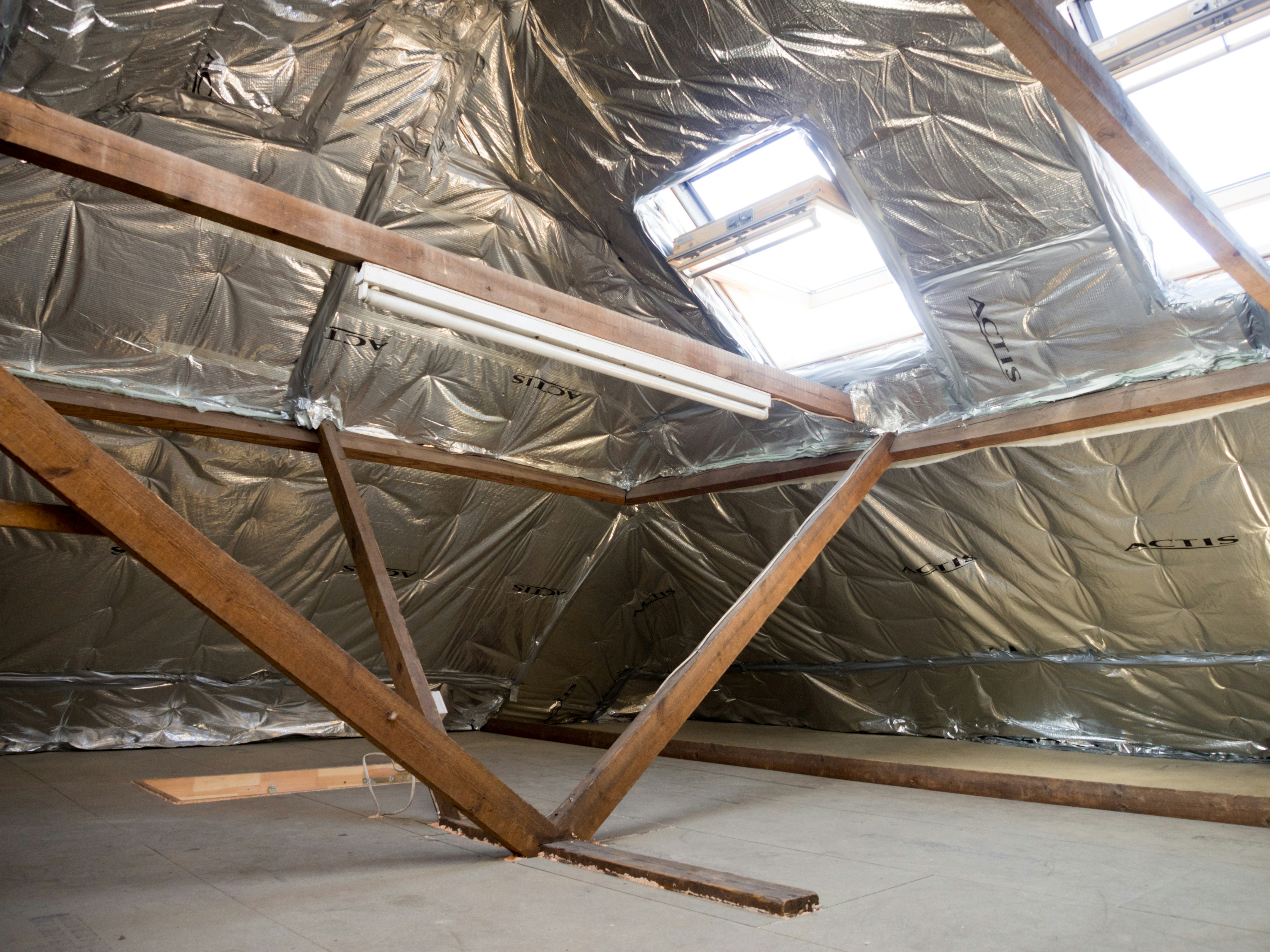 Attic interior with visible insulation, exposed beams, and skylight openings during a home improvement project.