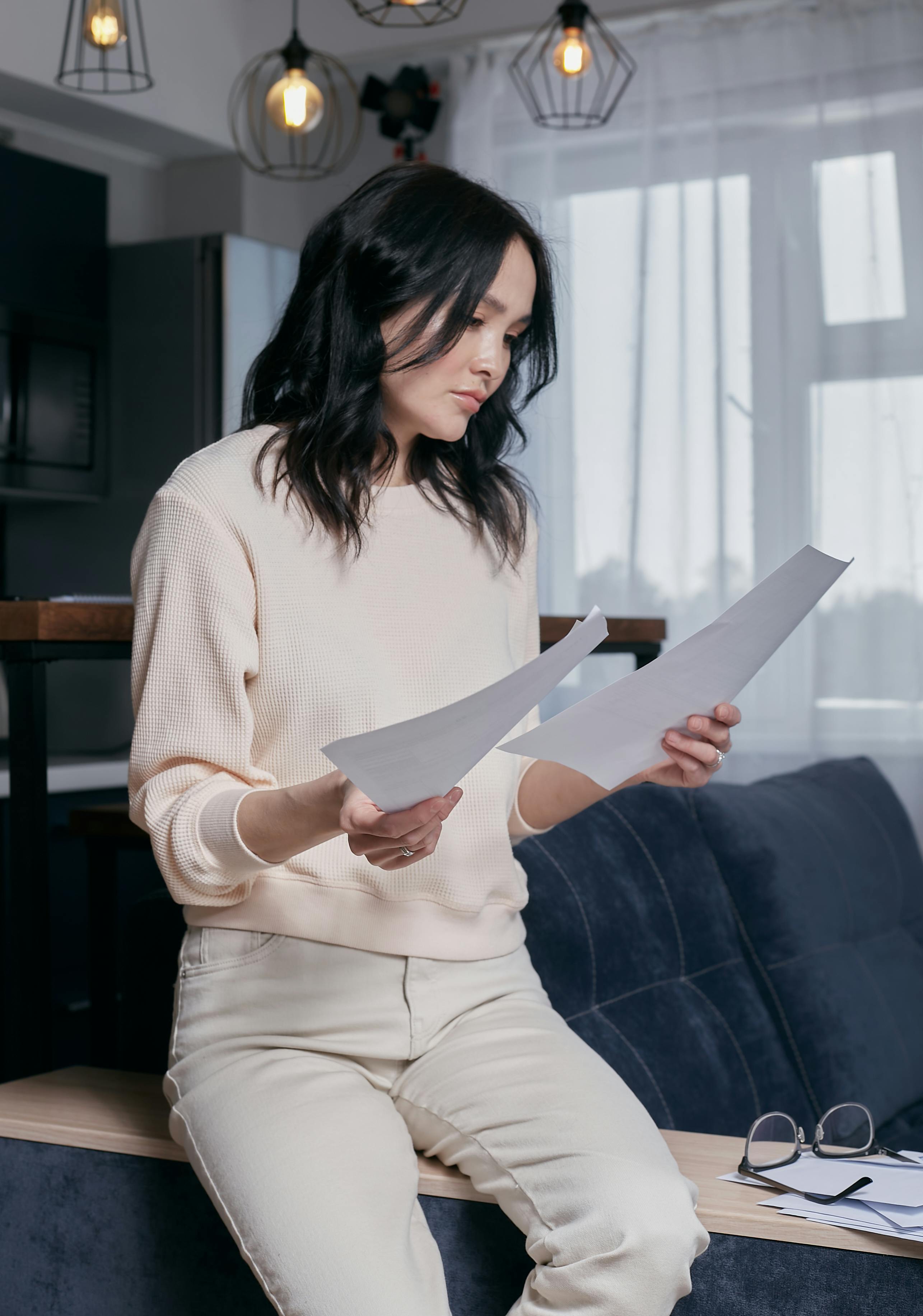 Woman sitting at home reading and reviewing documents with a focused expression