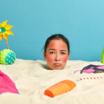 young-woman-head-with-sunscreen-cream-face-surrounded-by-beach-accessories (1)-303063cb