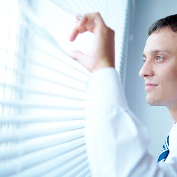 young-and-handsome-businessman-looking-out-of-the-window-through-the-blinds-SBI-305672534 (1)-fef48578