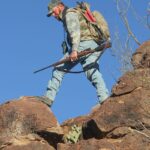 Man Climbing Rock with hunting shotgun-892d2a8c