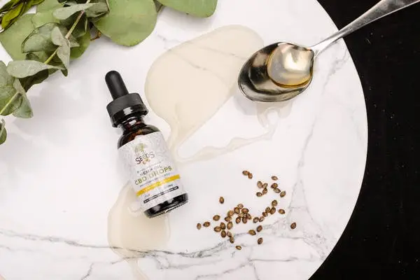 a bottle of CBD oil with a spoon and leaves on a table