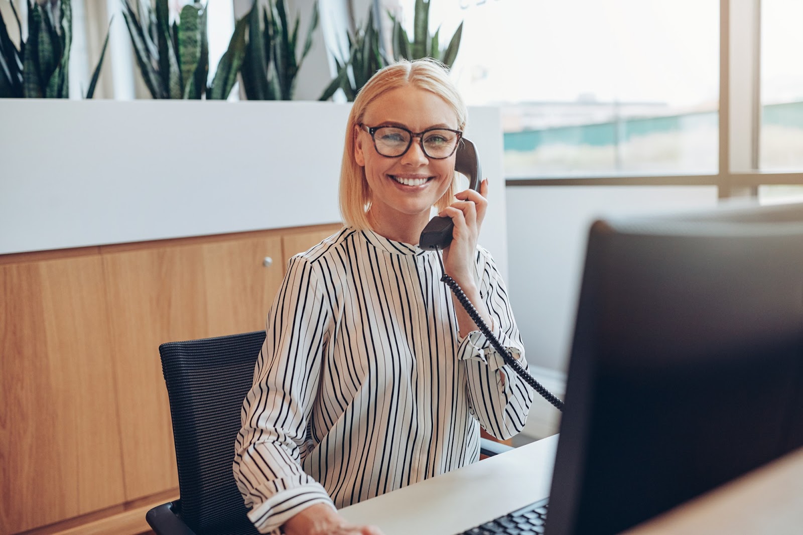 smiling-businesswoman-sitting-at-her-desk-talking-on-a-telephone-95a7ac05
