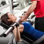 personal-trainer-helping-young-woman-lift-barbell-while-working-out-gym_662251-1130-6e01f854