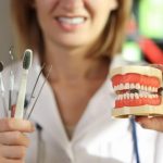 positive-dentist-holds-teeth-care-tools-human-jaws-model-clinic-office-doctor-presents (1)