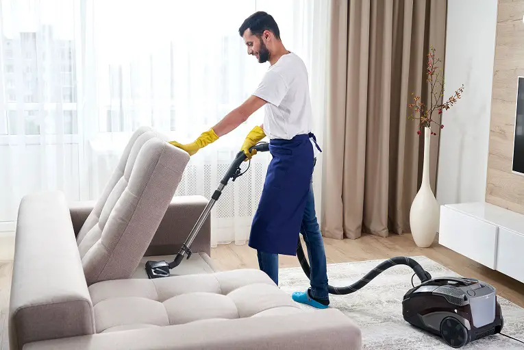 young-man-cleaning-sofa-with-vacuum-cleaner-leaving-room-home2