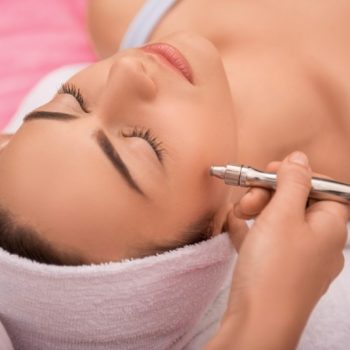 Close-up-top-view-side-view-portrait-of-a-young-woman-with-a-towel-on-her-head-lying-on-a-table-with-closed-eyes-getting-a-laser-skin-treatment-in-healthy-beauty-spa-salon