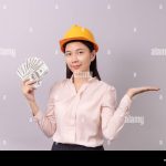 loans-for-real-estate-concept-woman-with-yellow-helmet-holding-banknote-money-in-right-hand-and-open-the-empty-palm-of-the-left-hand-TRXKFX