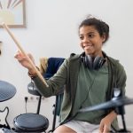 happy-cute-schoolgirl-with-drumsticks-hitting-drum-2021-12-16-00-28-52-utc