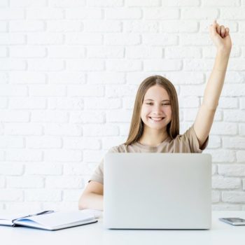 happy-teen-schoolgirl-studying-online-raising-her-arm-ready-for-answering-accomplish-exam-homework-768x659