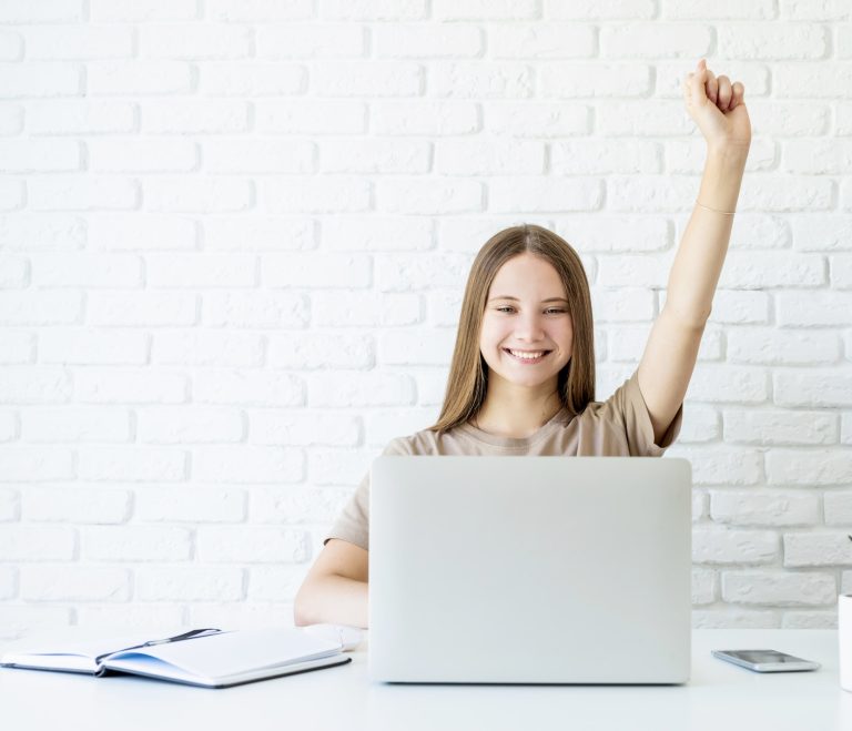 happy-teen-schoolgirl-studying-online-raising-her-arm-ready-for-answering-accomplish-exam-homework-768x659