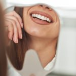 happy-young-woman-smiling-checking-out-her-perfect-healthy-teeth-mirror-close-up-dentist-office (1)