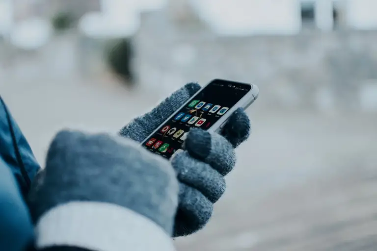 A person wearing gloves is using an iPhone. 