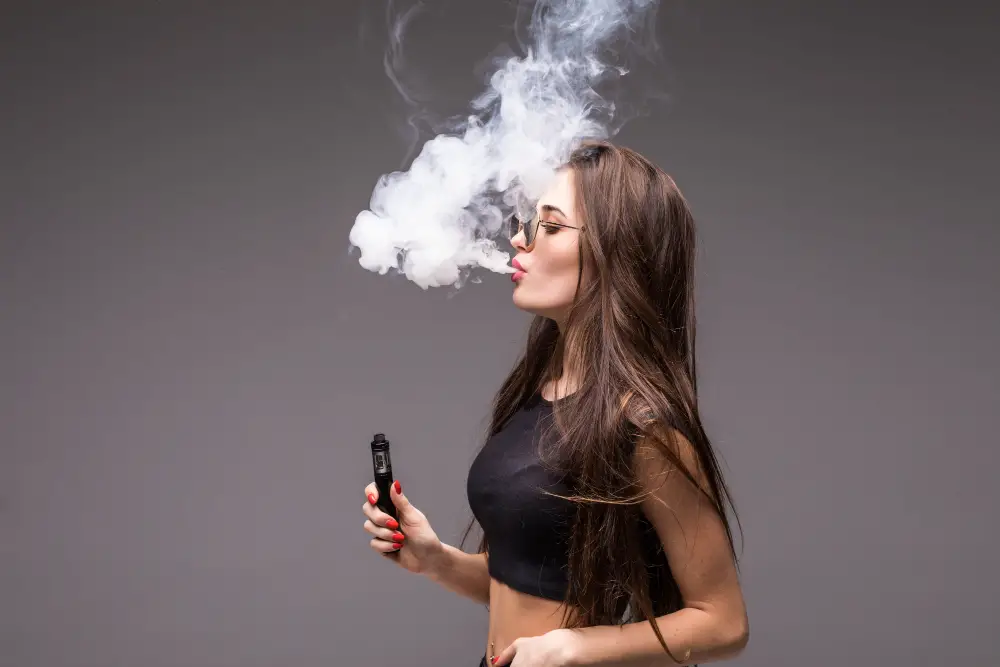 young-woman-sunglasses-black-clothes-vaping-blowing-smoke-electronic-cigarette-gray-wall