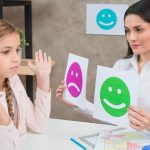 smiling-psychologist-showing-happy-sad-emotion-faces-cards-girl-child (1)