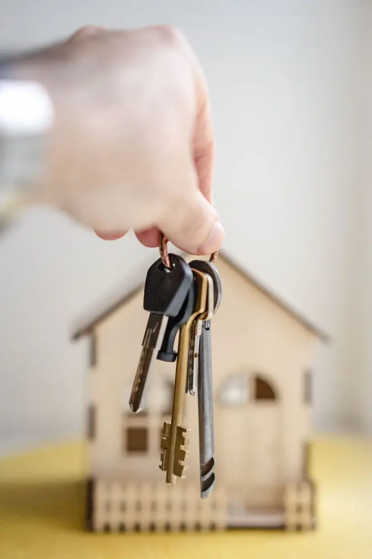 A photo showing a person holding keys in front of a miniature model of a house.