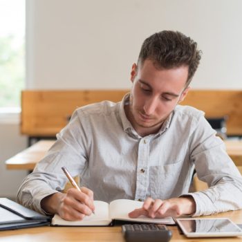 focused-male-student-doing-homework-desk-classroom-min