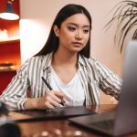 serious-brown-eyed-asian-woman-working-office-with-laptop-holding-pen_197531-19565