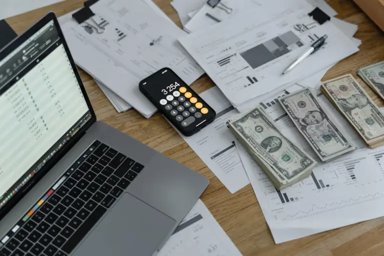 A desk setup with cash notes, a calculator, and a laptop