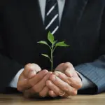 Image of a person in a suit is holding a small plant in his hands-min
