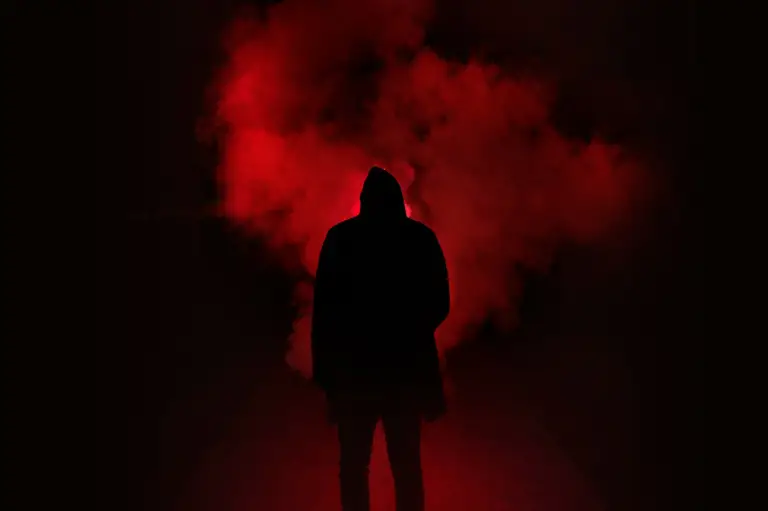 a man standing and smoke and red light in the background 