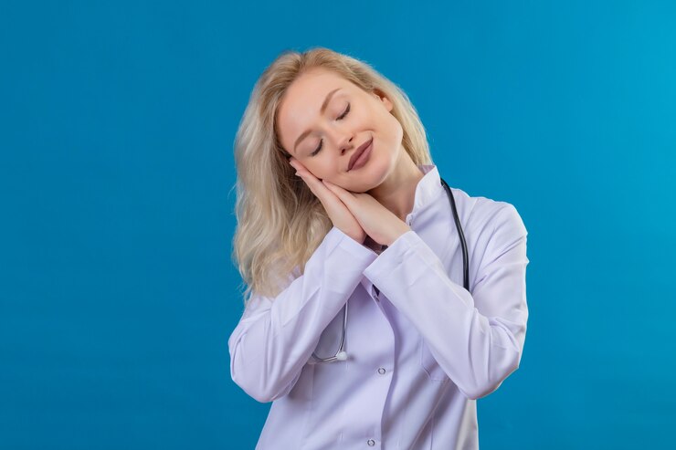 smiling-young-doctor-wearing-stethoscope-medical-gown-showing-sleep-gesture-blue-wall_141793-27145