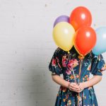 girl-holding-colorful-balloons-front-her-face-standing-against-wall_23-2148029658