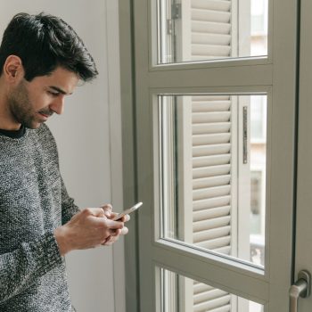 side-view-man-using-smartphone-near-window